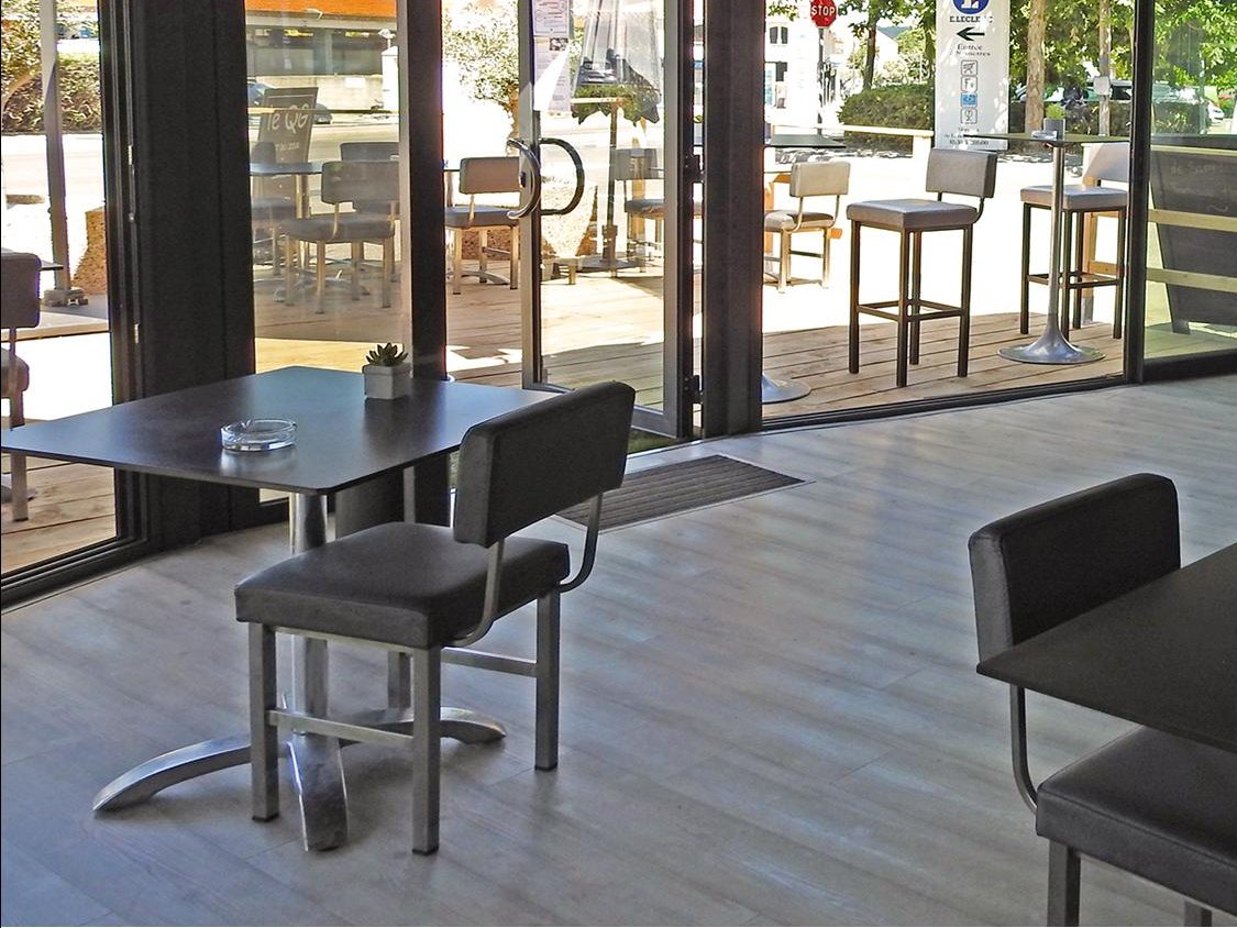 Une table et son fauteuil dans la salle, devant les grandes baies ouvertes sur la terrasse